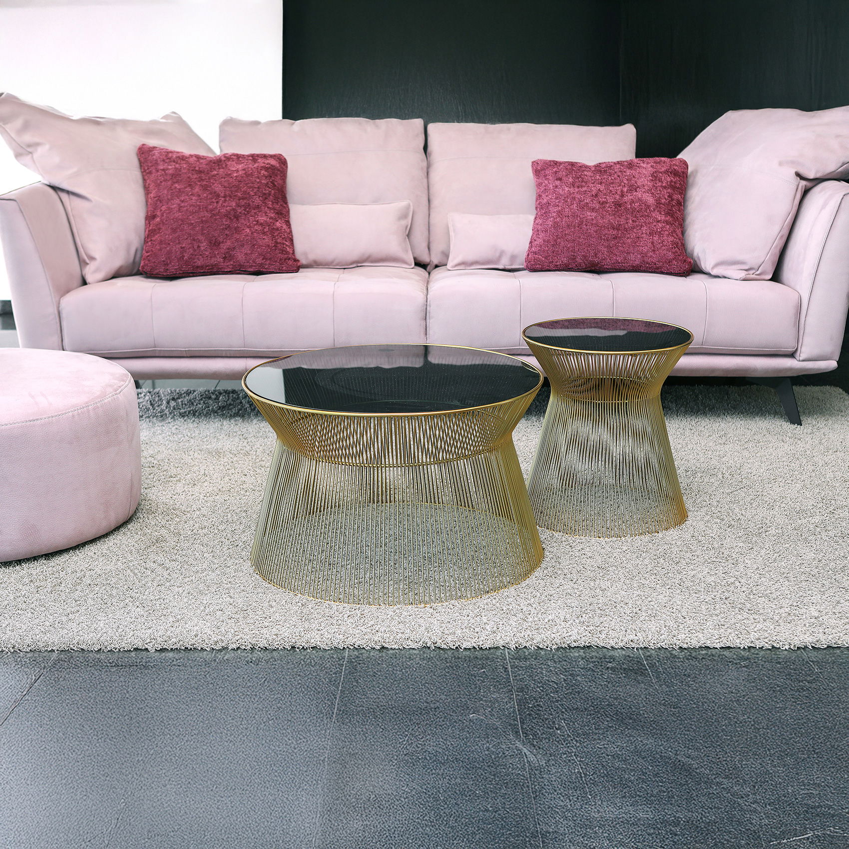 Wohnzimmer mit rosafarbenem Sofa, violetten Kissen und zwei goldenen Draht-Couchtischen mit dunkler Glasplatte auf hellem Teppich