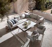 Moderner Gartentisch mit eleganter Glasplatte, umgeben von stilvollen, gepolsterten Stühlen und einem gemütlichen Ecksofa, aus der Vogelperspektive fotografiert.