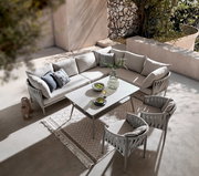 Moderner Gartentisch mit eleganter Glasplatte, umgeben von stilvollen, gepolsterten Stühlen und einem gemütlichen Ecksofa, aus der Vogelperspektive fotografiert.