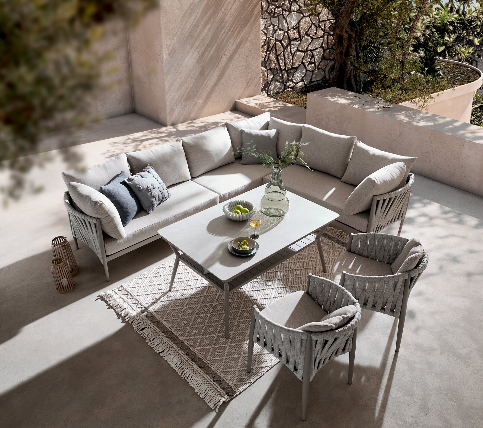 Moderner Gartentisch mit eleganter Glasplatte, umgeben von stilvollen, gepolsterten Stühlen und einem gemütlichen Ecksofa, aus der Vogelperspektive fotografiert.