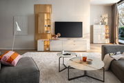 Moderne Wohnzimmer-Wandkombination mit Holz- und Weißtönen, bestehend aus einem TV-Schrank und einem hohen Regal mit Beleuchtung, aus der Perspektive des Wohnzimmers betrachtet.