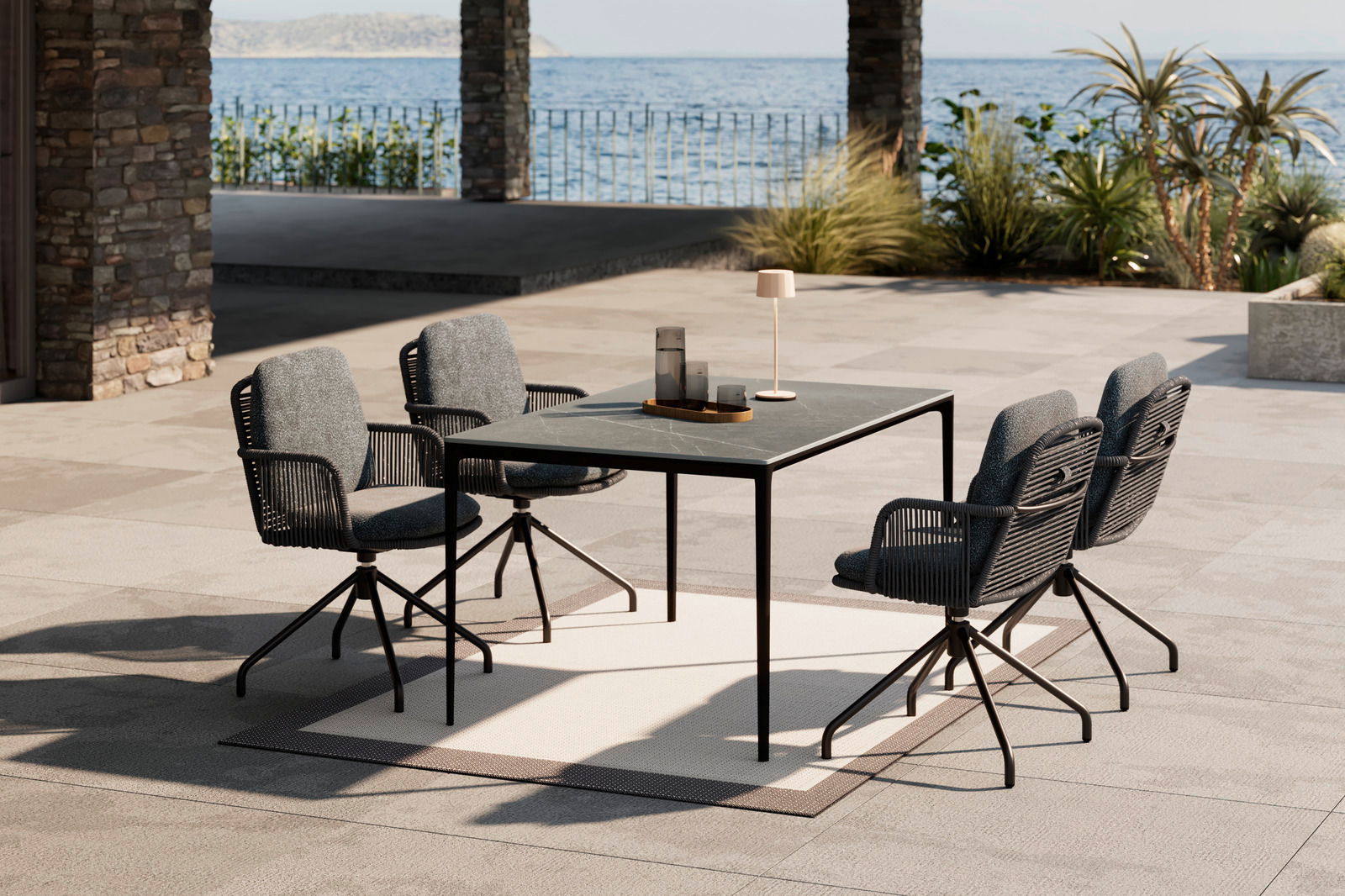 Moderner Gartentisch mit vier Stühlen auf einer Terrasse mit Meerblick, seitliche Perspektive.