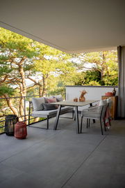 Moderne Outdoor-Lounge mit 2-Sitzer und Eckelement auf einer Terrasse mit Blick auf Bäume, aus seitlicher Perspektive.