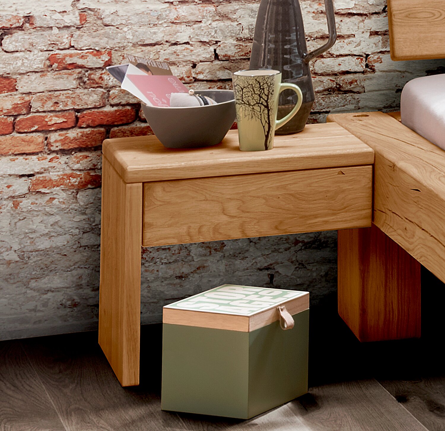 Holz-Nachtkommode mit Schublade, dekoriert mit Tasse und Schale, vor einer Ziegelwand, seitliche Perspektive