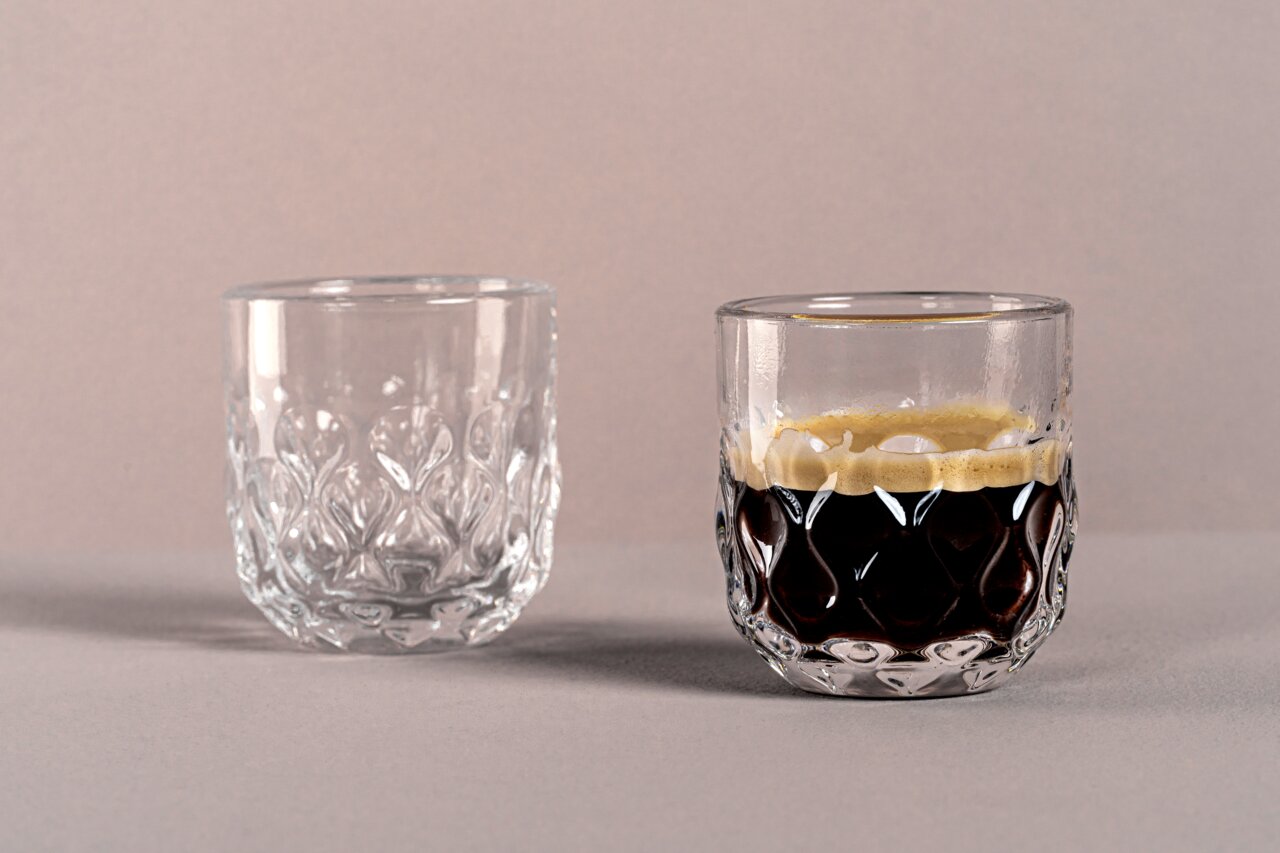 Twee elegante espressoglazen met een gestructureerd ontwerp, waarvan één gevuld met espresso, gefotografeerd vanuit een zijaanzicht.