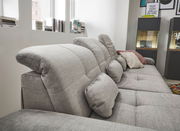 Graues Sofa mit verstellbaren Kopfstützen und mehreren Kissen, seitliche Perspektive.