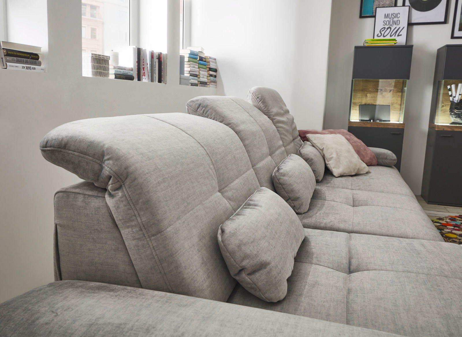 Graues Sofa mit verstellbaren Kopfstützen und mehreren Kissen, seitliche Perspektive.