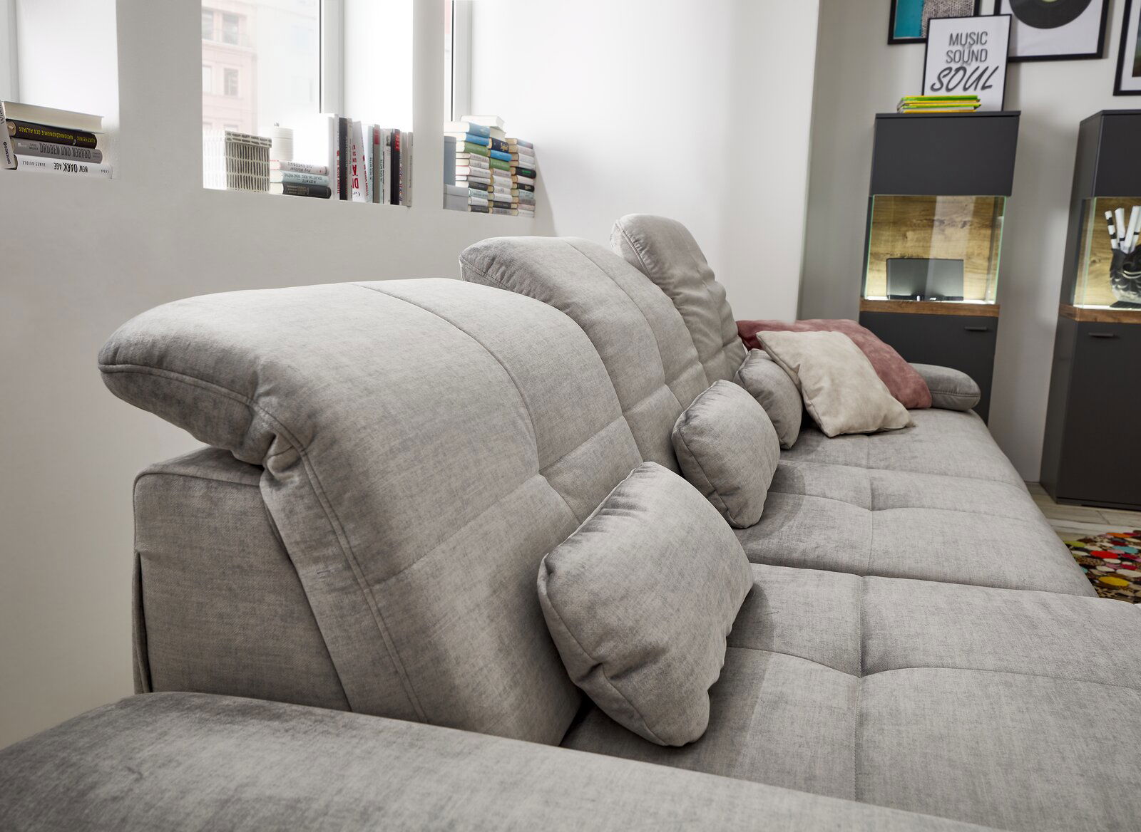 Graues Sofa mit verstellbaren Kopfstützen und mehreren Kissen, seitliche Perspektive.