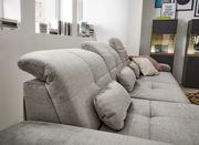 Graues Sofa mit verstellbaren Kopfstützen und mehreren Kissen, seitliche Perspektive.