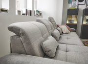 Graues Sofa mit verstellbaren Kopfstützen und mehreren Kissen, seitliche Perspektive.
