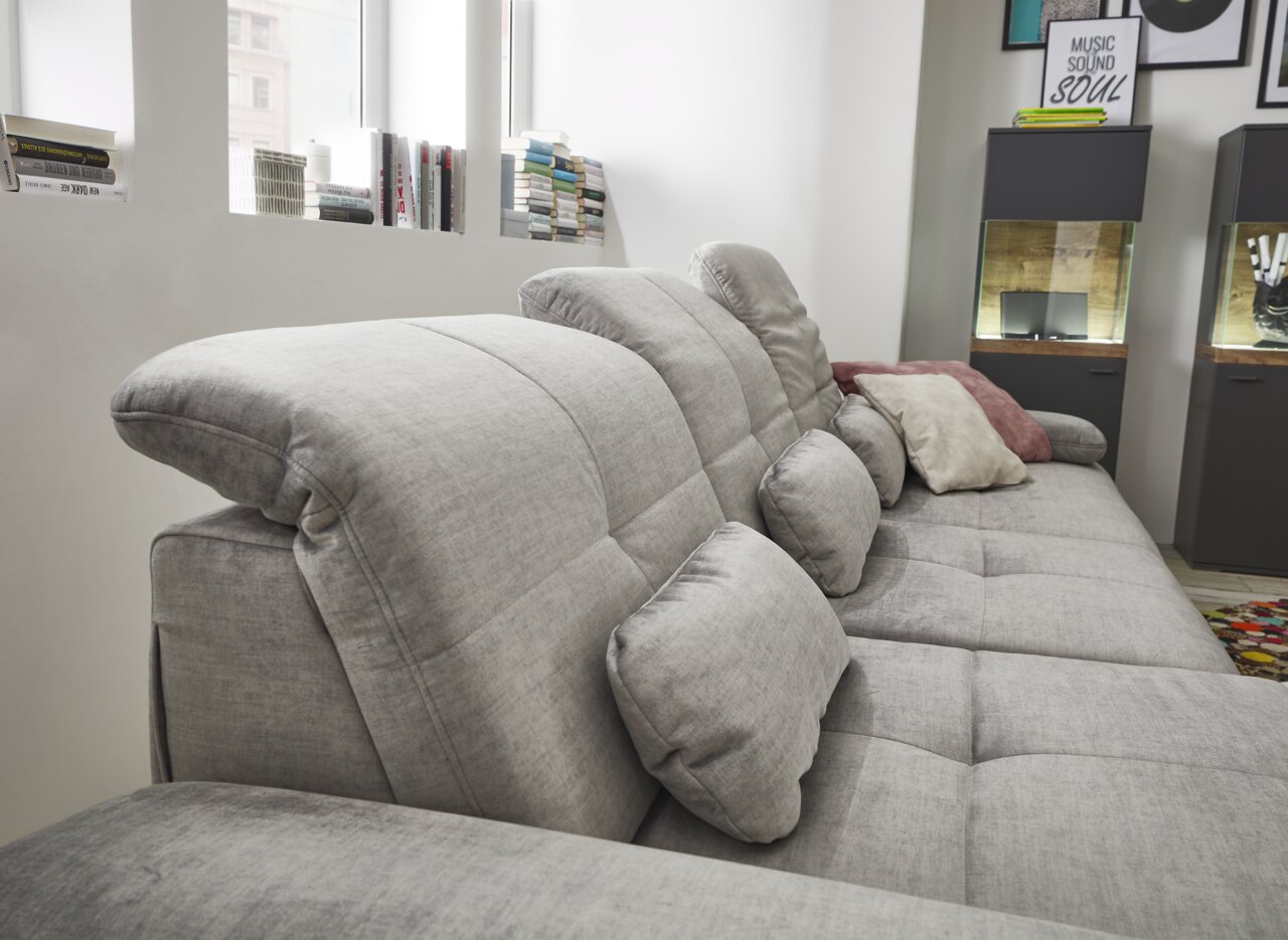 Graues Sofa mit verstellbaren Kopfstützen und mehreren Kissen, seitliche Perspektive.