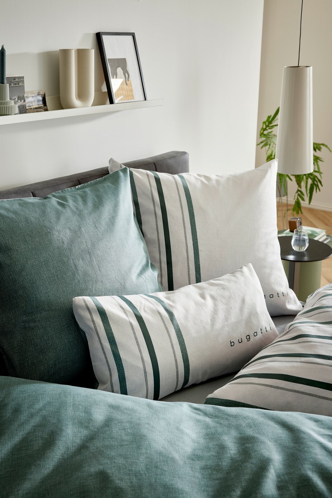 Close-up schuin vooraanzicht van Bugatti beddengoed met wit-groen gestreepte kussens en groen dekbedovertrek op een grijs bed in een modern interieur
