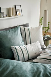 Close-up schuin vooraanzicht van Bugatti beddengoed met wit-groen gestreepte kussens en groen dekbedovertrek op een grijs bed in een modern interieur