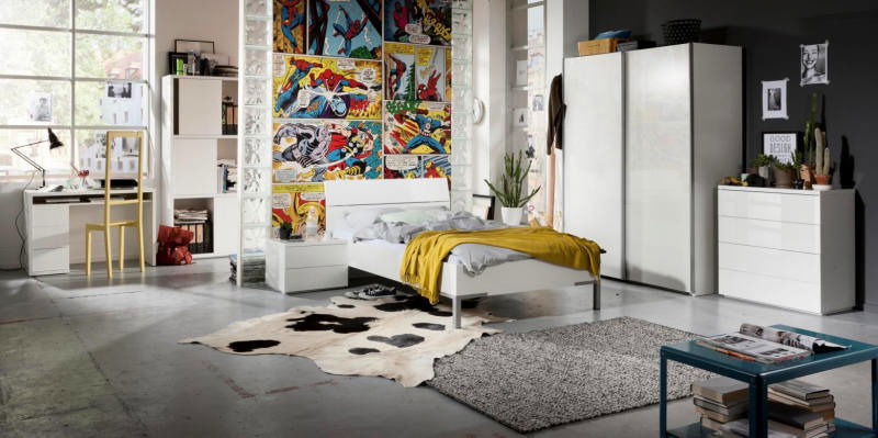 Modernes Schlafzimmer mit einem weißen Bett im Vordergrund, umgeben von stilvollen Möbeln und einer auffälligen Comic-Wand im Hintergrund. Perspektive: seitliche Ansicht des Bettes.