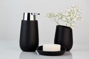 Schwarzer Keramik-Seifenspender mit glänzendem Chrom-Pumpkopf, frontal fotografiert, neben einer passenden Vase mit weißen Blumen und einer Seifenschale.
