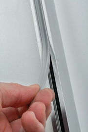 Nahaufnahme einer Hand, die eine transparente Sicherheitsabdeckung in eine Metallschiene einfügt, seitliche Perspektive.