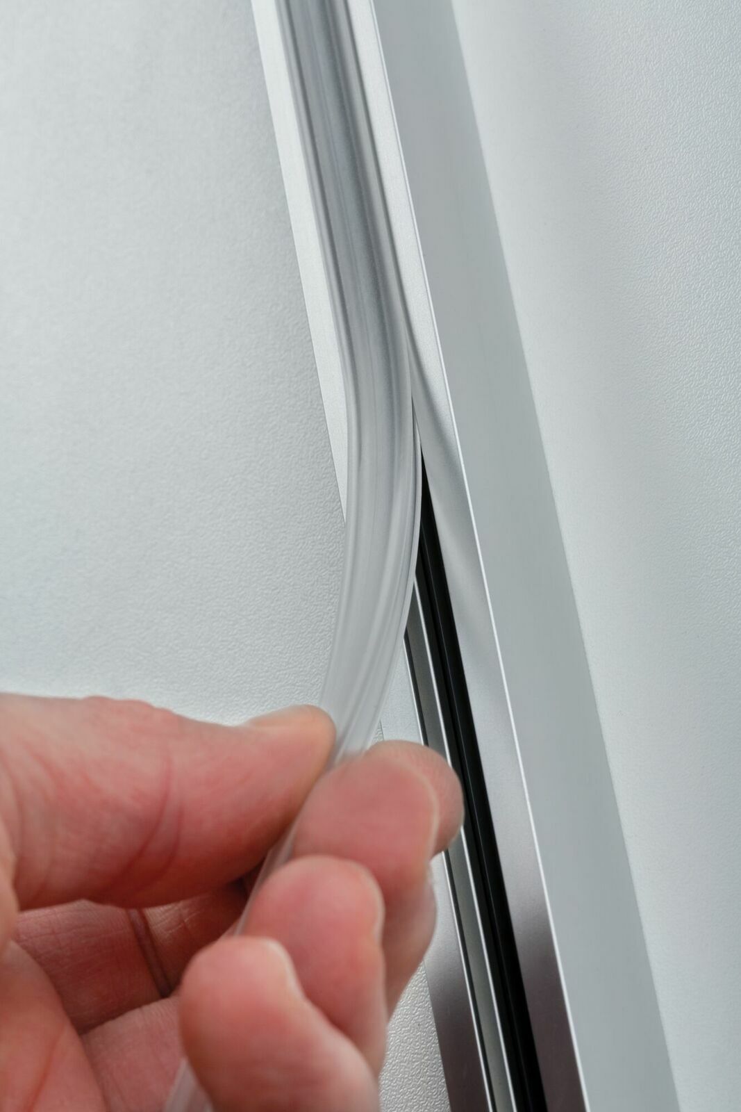 Nahaufnahme einer Hand, die eine transparente Sicherheitsabdeckung in eine Metallschiene einfügt, seitliche Perspektive.