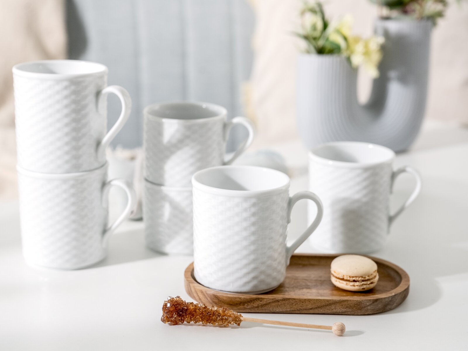 Creatable Kaffeebecher 6-tlg POLO Weiße Keramik-Kaffeetassen mit feiner Reliefstruktur und Henkel auf hellem Tisch, eine Tasse auf Holztablett mit Macaron; Perspektive: leicht erhöhte Frontansicht.