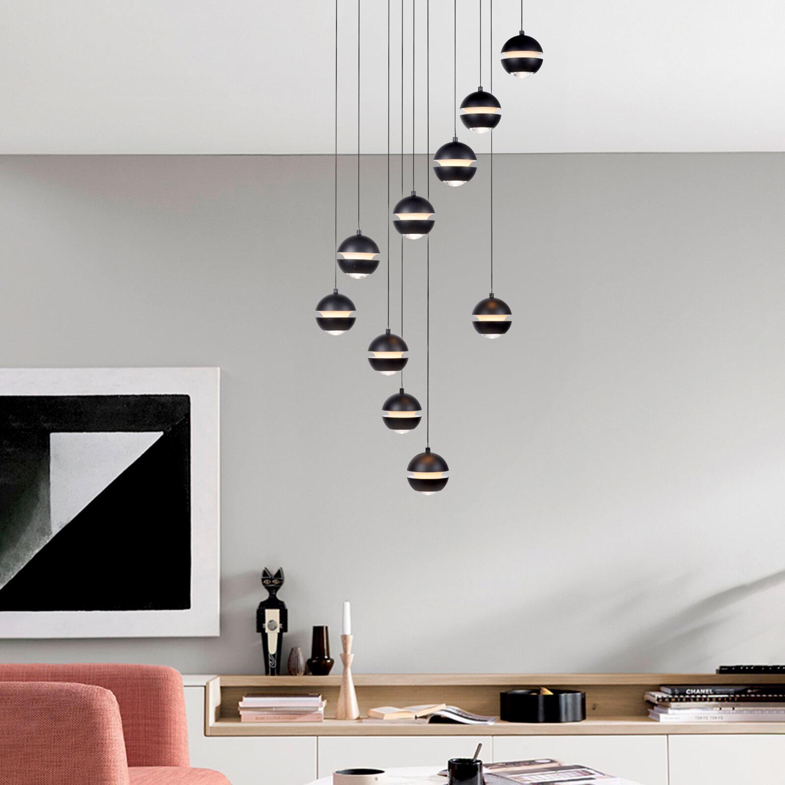 Hanglamp met meerdere lampen, voorzien van zwarte, bolvormige kappen en een lichtband rondom, in een verspringende opstelling boven een moderne woonkamer; vooraanzicht van de ruimte, licht van onderaf.