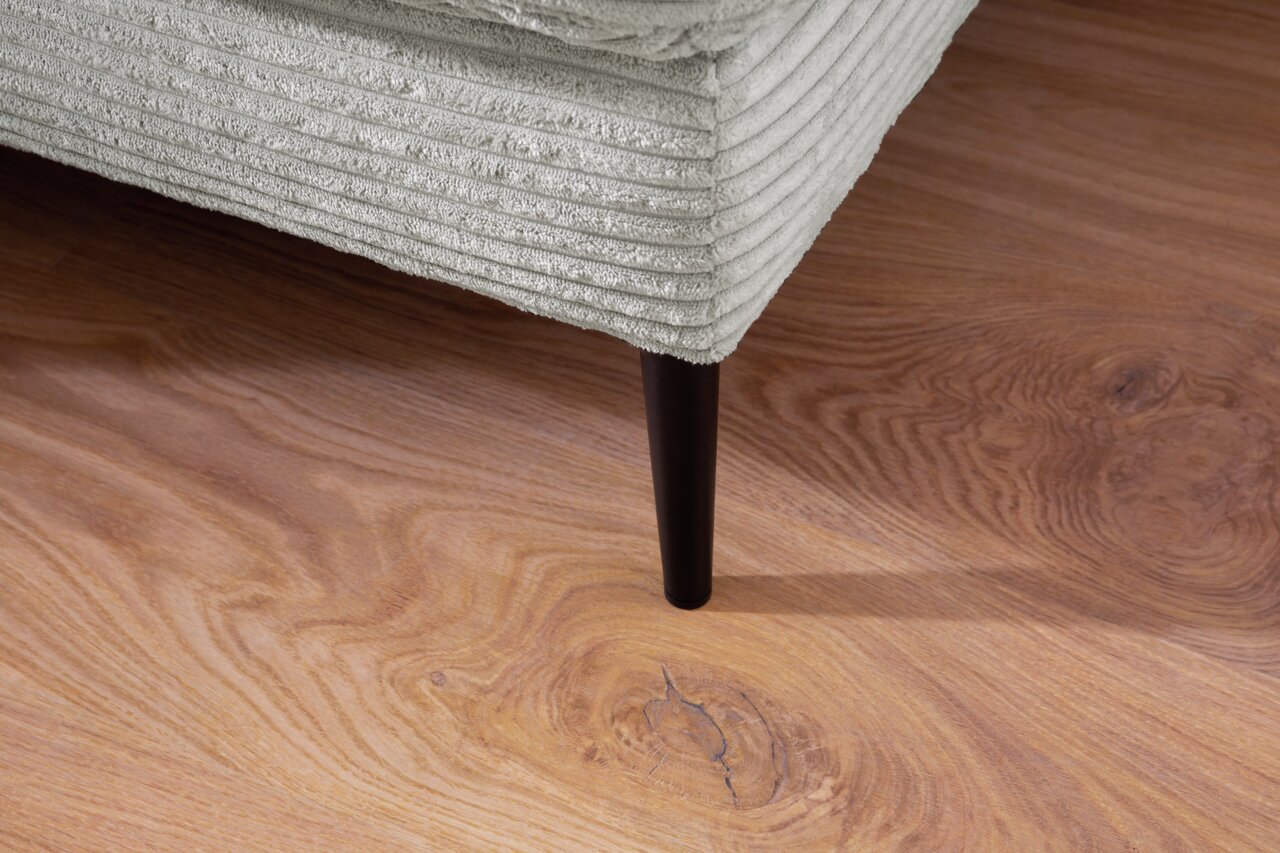 Nahaufnahme eines Longchairs mit geripptem Stoffbezug und schwarzem Bein auf Holzfußboden, Perspektive von unten.