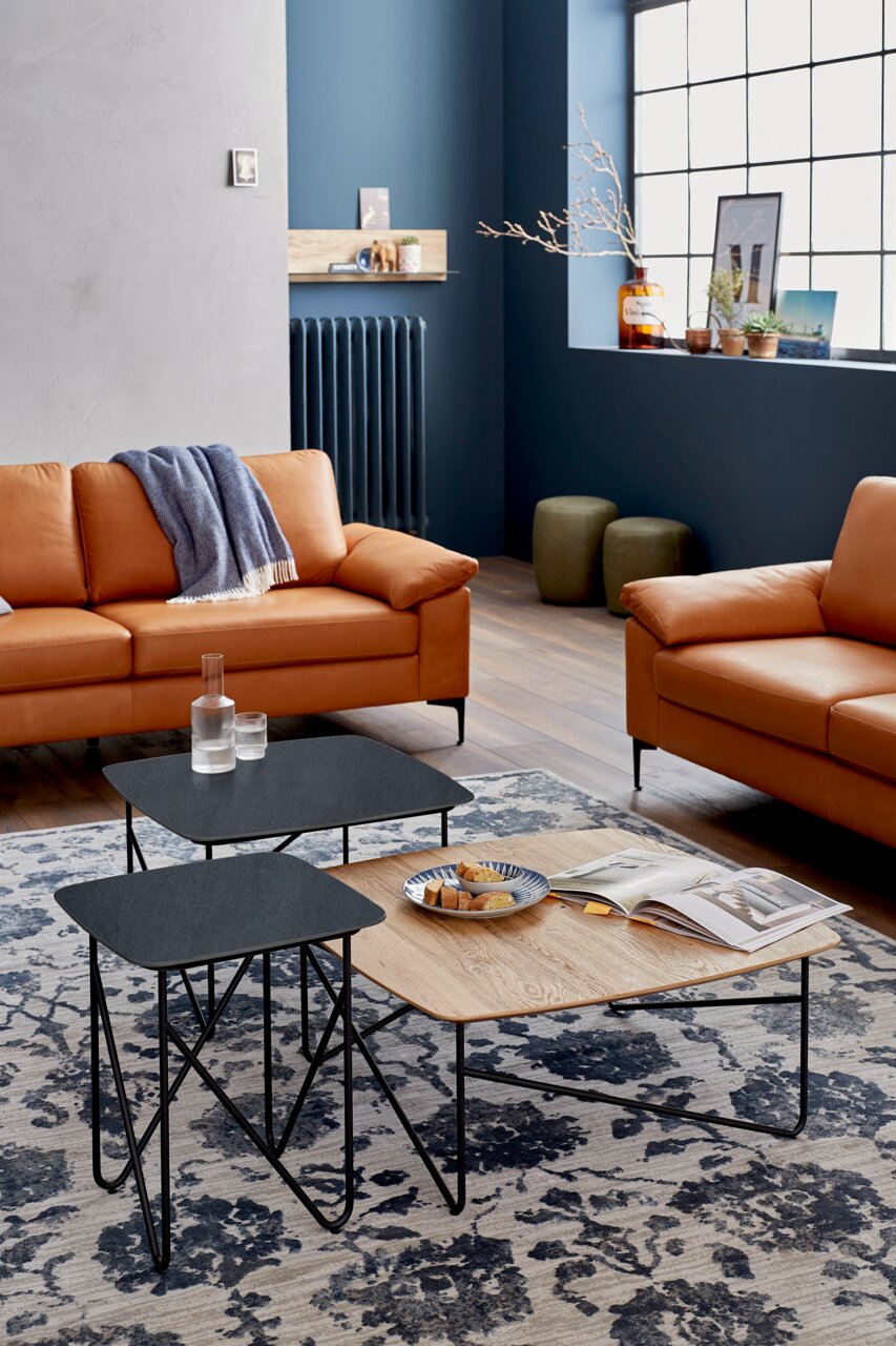 Moderner Couchtisch mit schwarzer und holzfarbener Oberfläche, aus der Perspektive eines gemütlichen Wohnzimmers mit Ledersofas und dekorativem Teppich.