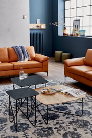 Moderne salontafel met een zwart en houtkleurig oppervlak, gezien vanuit een gezellige woonkamer met leren banken en een decoratief tapijt.