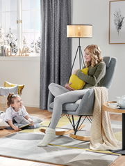 Gemütlicher Stillstuhl in einem modernen Wohnzimmer, seitliche Perspektive, mit einer Frau, die ein Kissen hält, und einem Kind, das auf dem Boden sitzt.