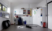 Mehrzweckschränke und Regale in einer Garage, frontal fotografiert. Die Schränke sind weiß und bieten Stauraum für verschiedene Haushaltsgegenstände.