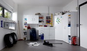 Mehrzweckschränke und Regale in einer Garage, frontal fotografiert. Die Schränke sind weiß und bieten Stauraum für verschiedene Haushaltsgegenstände.