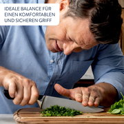 Mann in blauer Hemd schneidet Kräuter auf einem Holzbrett mit einem Messer, Nahaufnahme.
