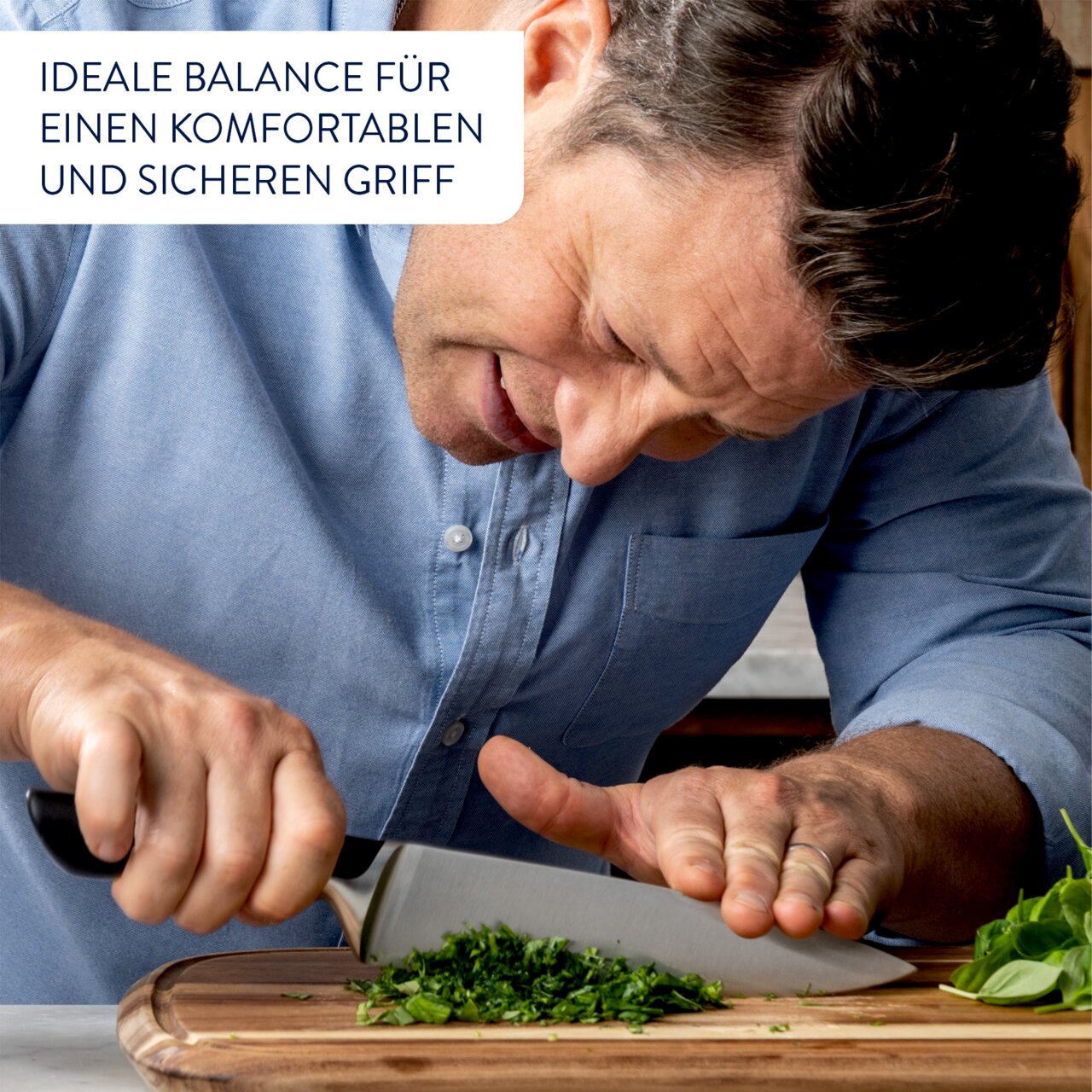 Mann in blauer Hemd schneidet Kräuter auf einem Holzbrett mit einem Messer, Nahaufnahme.