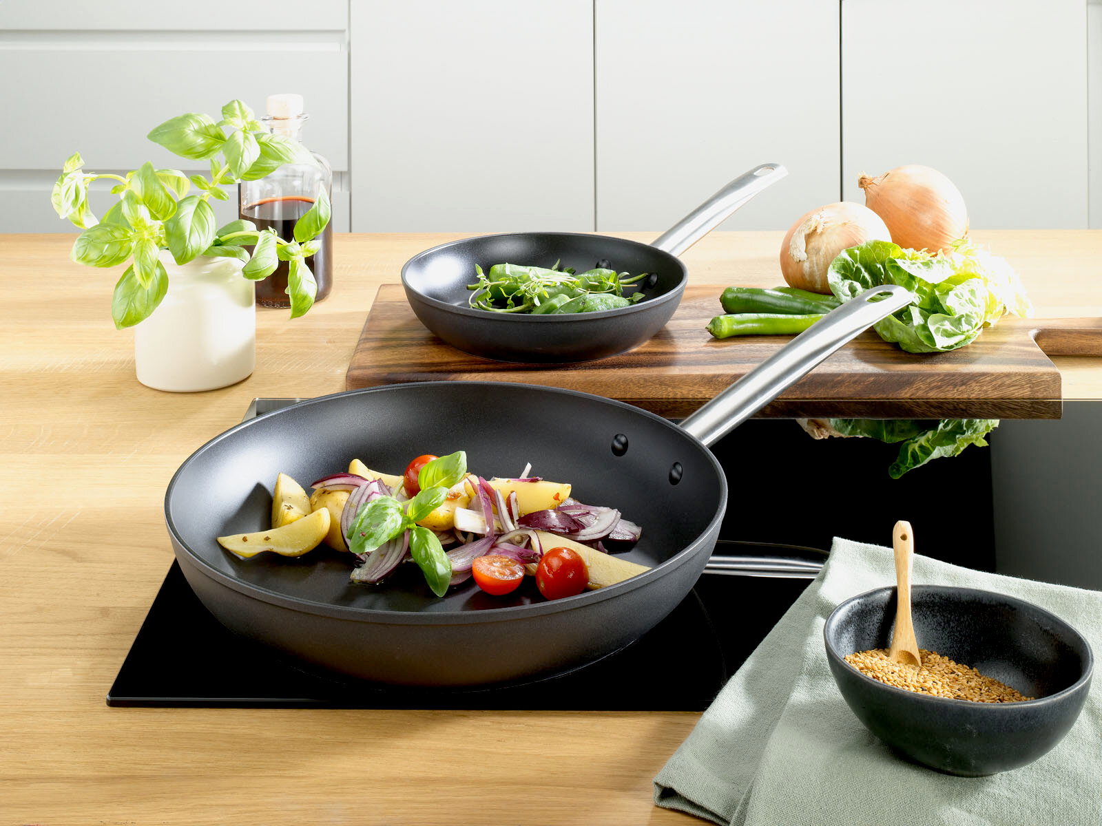 Homeware Pfannenset Zwei schwarze Pfannen auf einem Herd, gefüllt mit frischem Gemüse, aus der Vogelperspektive fotografiert.