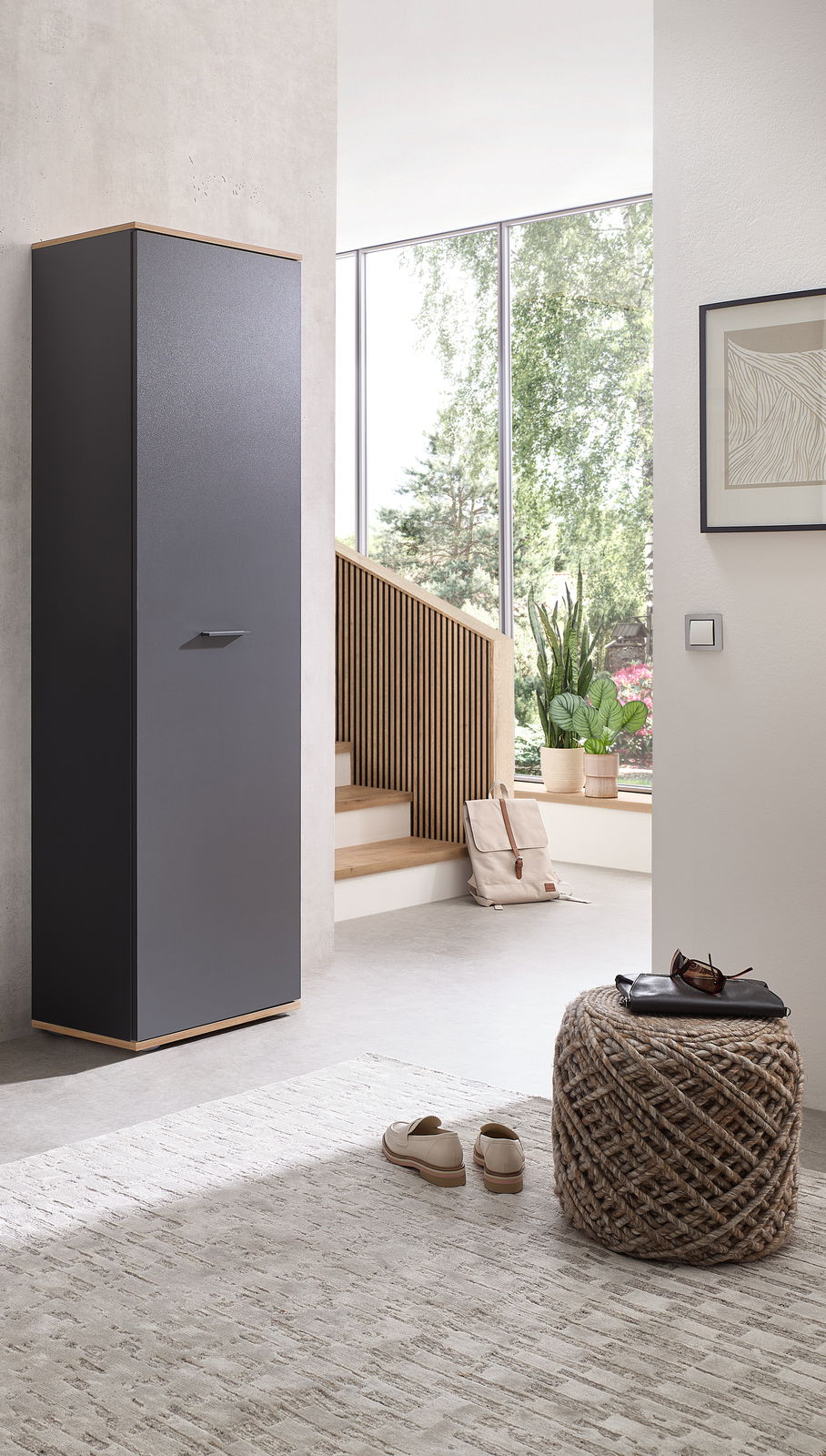 Moderner Hochschrank in dunklem Design, seitliche Perspektive, in einem hellen Raum mit großen Fenstern und minimalistischer Einrichtung.