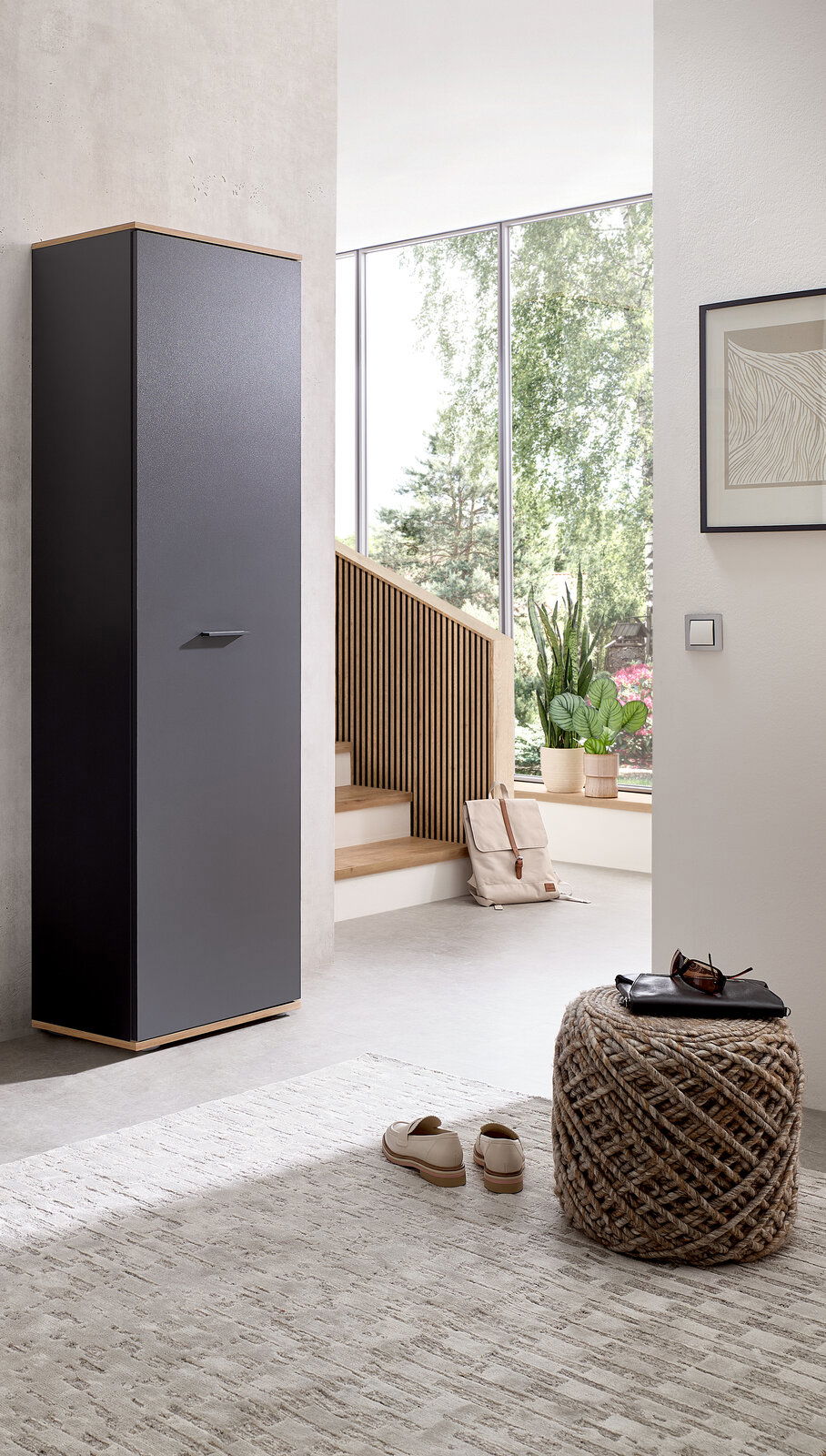 XORA Hochschrank FYNN Moderner Hochschrank in dunklem Design, seitliche Perspektive, in einem hellen Raum mit großen Fenstern und minimalistischer Einrichtung.