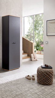 Moderner Hochschrank in dunklem Design, seitliche Perspektive, in einem hellen Raum mit großen Fenstern und minimalistischer Einrichtung.