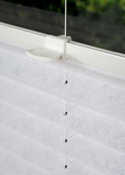 Nahaufnahme eines weißen, gefädelten Plissees an einem Fenster, seitliche Perspektive