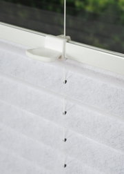 Nahaufnahme eines weißen, gefädelten Plissees an einem Fenster, seitliche Perspektive