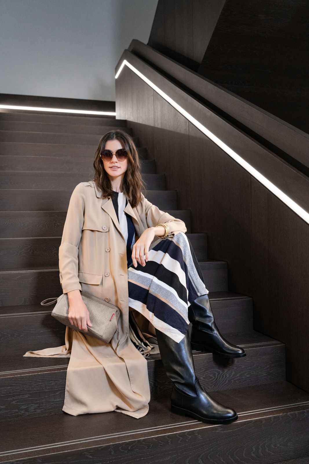 Frau sitzt auf einer Treppe mit einer beigen Tasche in der Hand, seitliche Perspektive