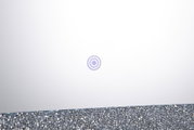 Weiße, minimalistische Produktoberfläche mit kleinem kreisförmigem Symbol in der Mitte und glitzerndem Rand am unteren Bildrand, Nahaufnahme in frontaler Draufsicht