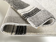 Nahaufnahme eines gefalteten Teppichs mit grauen und schwarzen Streifen, Perspektive von der Seite.