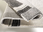 Nahaufnahme eines gefalteten Teppichs mit grauen und schwarzen Streifen, Perspektive von der Seite.