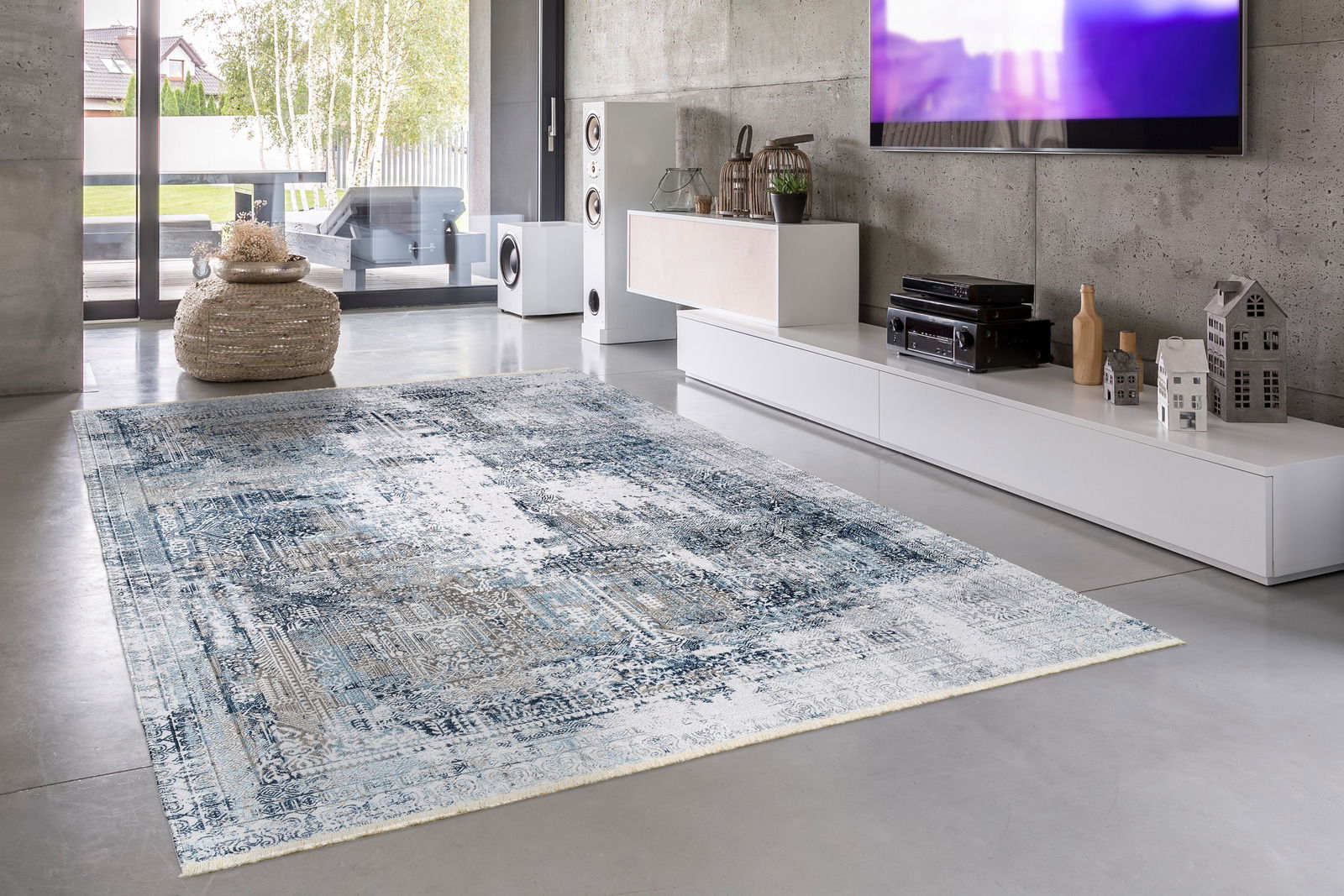 Moderner Wohnzimmerteppich in Blau- und Grautönen auf Betonboden, mit Blick auf eine stilvolle Einrichtung und große Fenster im Hintergrund.