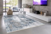 Moderner Wohnzimmerteppich in Blau- und Grautönen auf Betonboden, mit Blick auf eine stilvolle Einrichtung und große Fenster im Hintergrund.