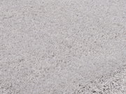 Nahaufnahme eines weichen, hellgrauen Teppichs mit flauschiger Textur, perspektivisch von der Seite aufgenommen.