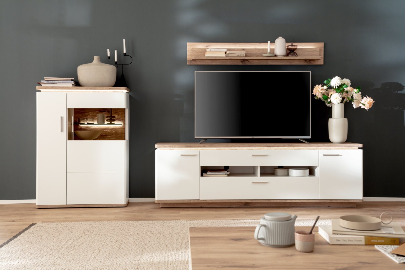 Stylife Tv-kast PALERMO Moderne woonkamerinrichting met een wit tv-lowboard en bijpassende vitrinekast met houten accenten, tv en wandplank voor een donkergrijze muur, gezien vanaf de voorkant.