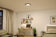 Moderne quadratische LED-Deckenleuchte in Schwarz mit warmweißem Licht, montiert an weißer Zimmerdecke in Schlafzimmer/Homeoffice-Umgebung, Perspektive: Blick schräg von unten nach oben