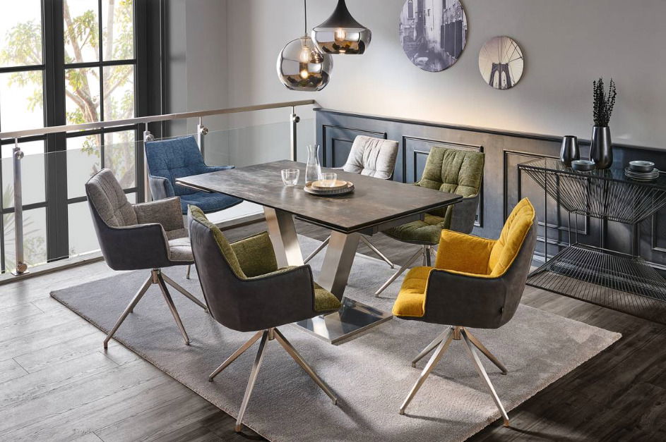 Moderner Esstisch mit Metallgestell und dunkler Tischplatte, umgeben von bunten Stühlen in einem stilvollen Esszimmer. Perspektive von schräg oben.