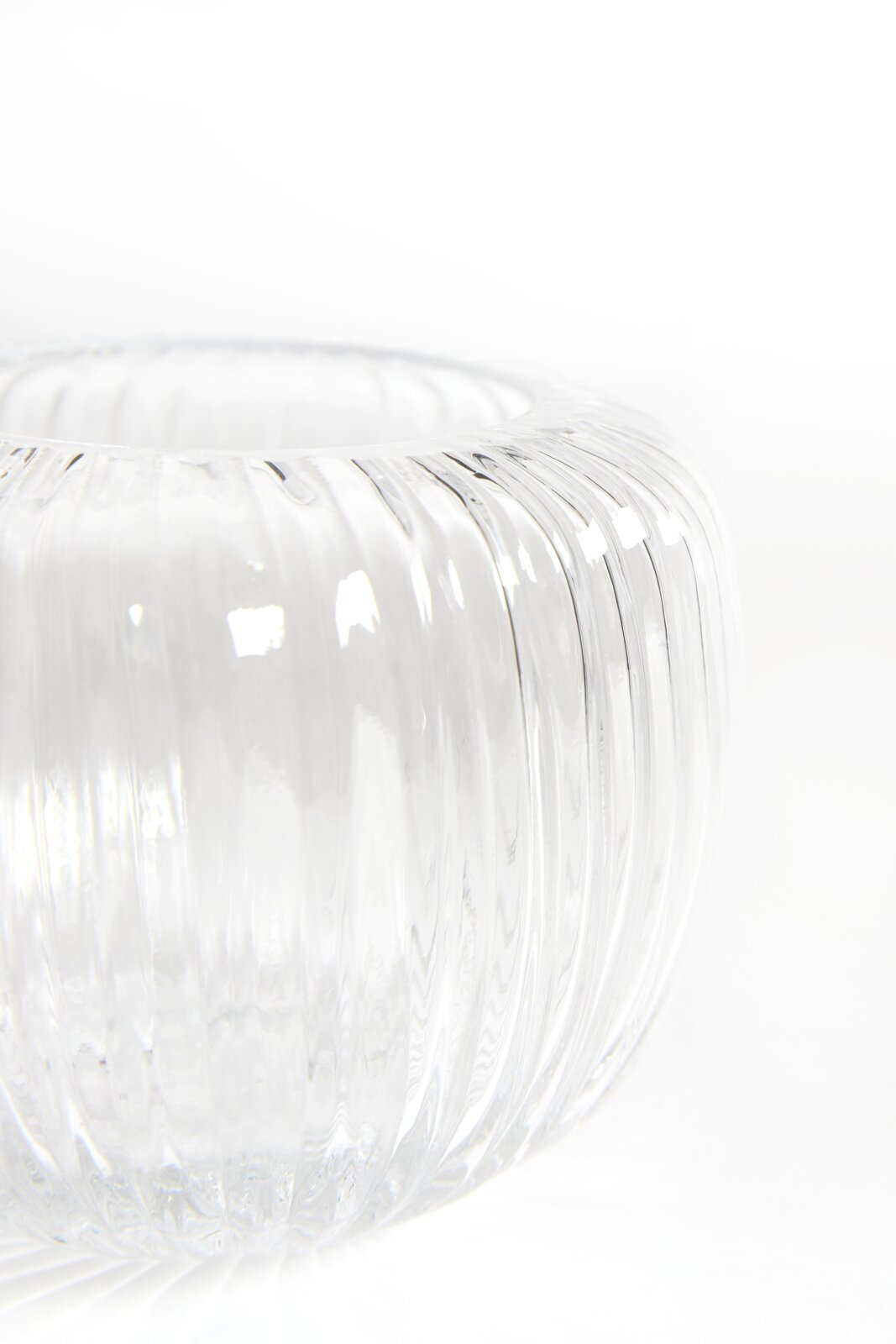 Nahaufnahme eines transparenten, bauchigen Glasgefäßes mit vertikaler Rillenstruktur, aus leicht erhöhter seitlicher Perspektive vor weißem Hintergrund