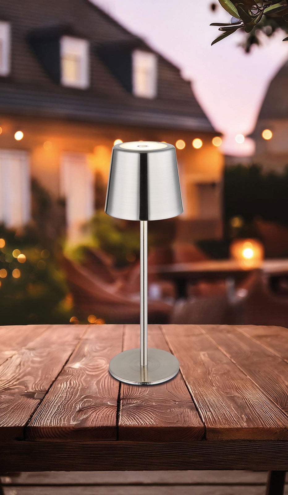 Moderne Tischleuchte aus Metall auf einem Holztisch, im Freien bei Dämmerung fotografiert.