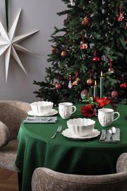 Frühstücksset auf einem festlich gedeckten Tisch mit grünem Tischtuch, im Hintergrund ein geschmückter Weihnachtsbaum. Perspektive von vorne.